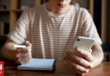 a14414fc young man writing something notebook while looking his smartphone og.jpg