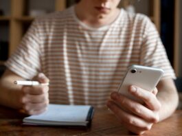 a14414fc young man writing something notebook while looking his smartphone og.jpg