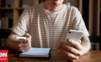 a14414fc young man writing something notebook while looking his smartphone og.jpg