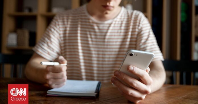 a14414fc young man writing something notebook while looking his smartphone og.jpg